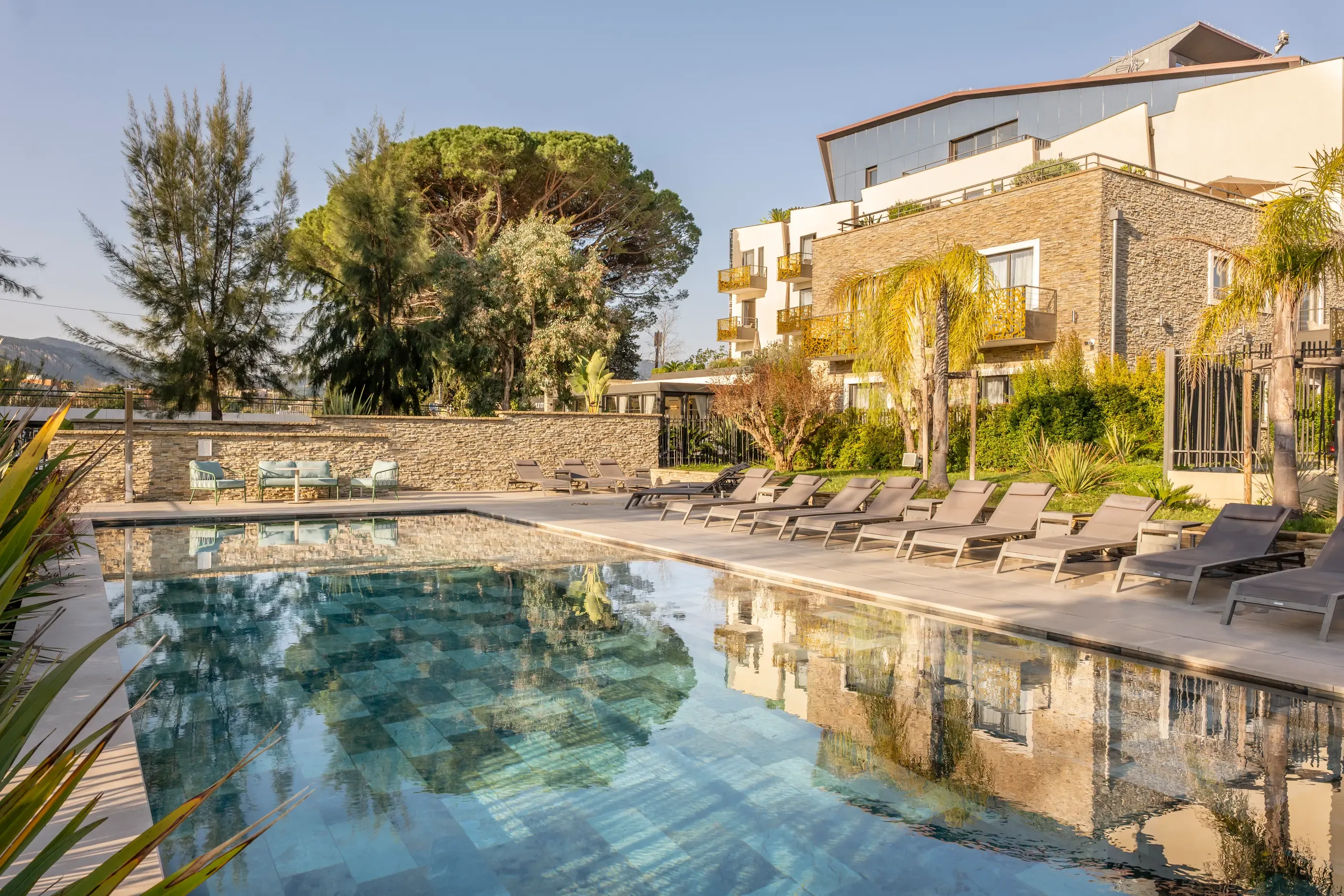 Piscine entourée de transats avec un bâtiment en pierre et des arbres en arrière-plan