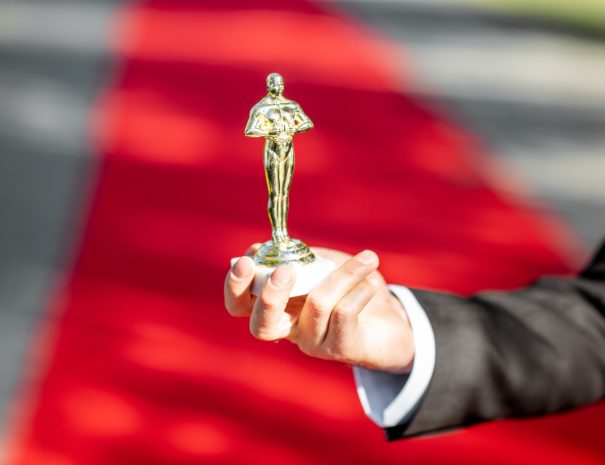 Man holding famous film award statue on the red carpet background, close-up view