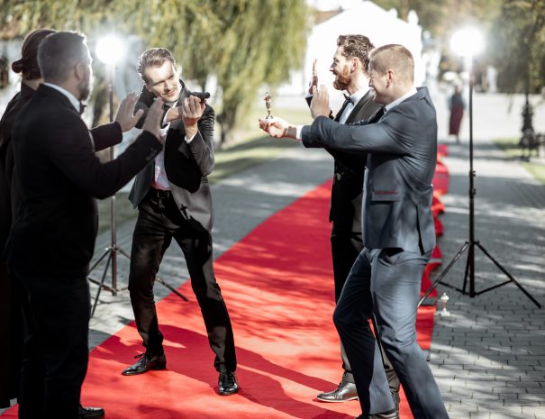 Group of a men as a well-known movie actors and secret agent playing with handgun during awards ceremony on the red carpet outdoors